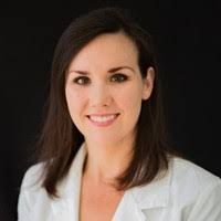 Smiling professional in a white blazer against a dark background