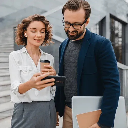 Two coworkers checking a phone and tablet outside a modern office building
