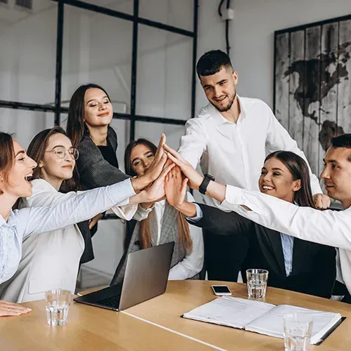 Team meeting in a modern office, coworkers stacking hands in a group high-five around a conference table.