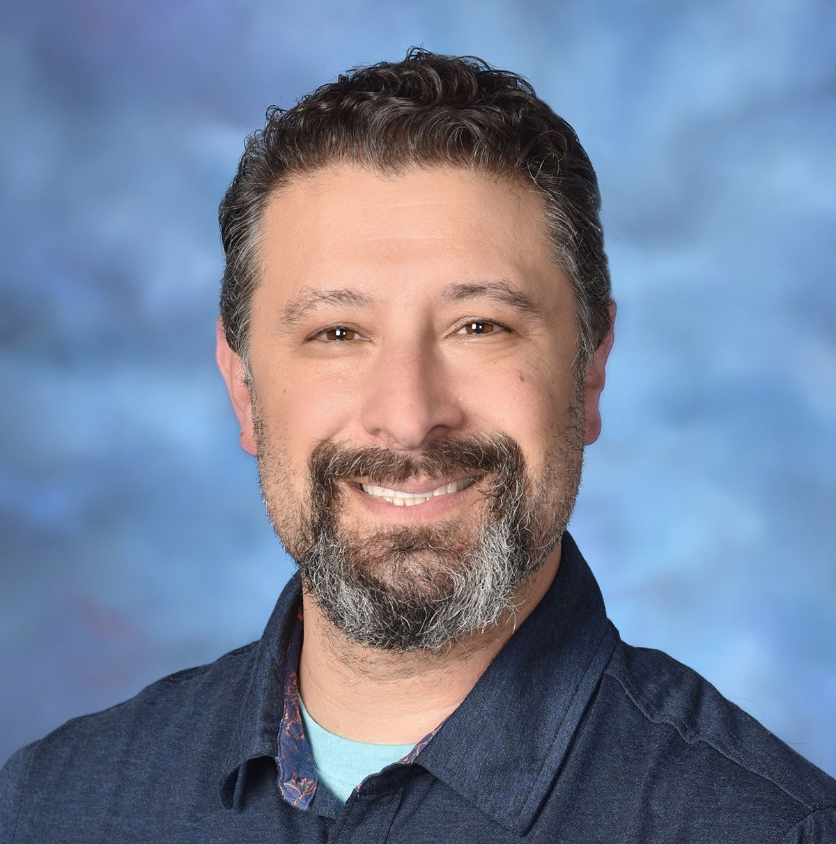 Smiling man in a dark blue shirt against a soft blue studio background