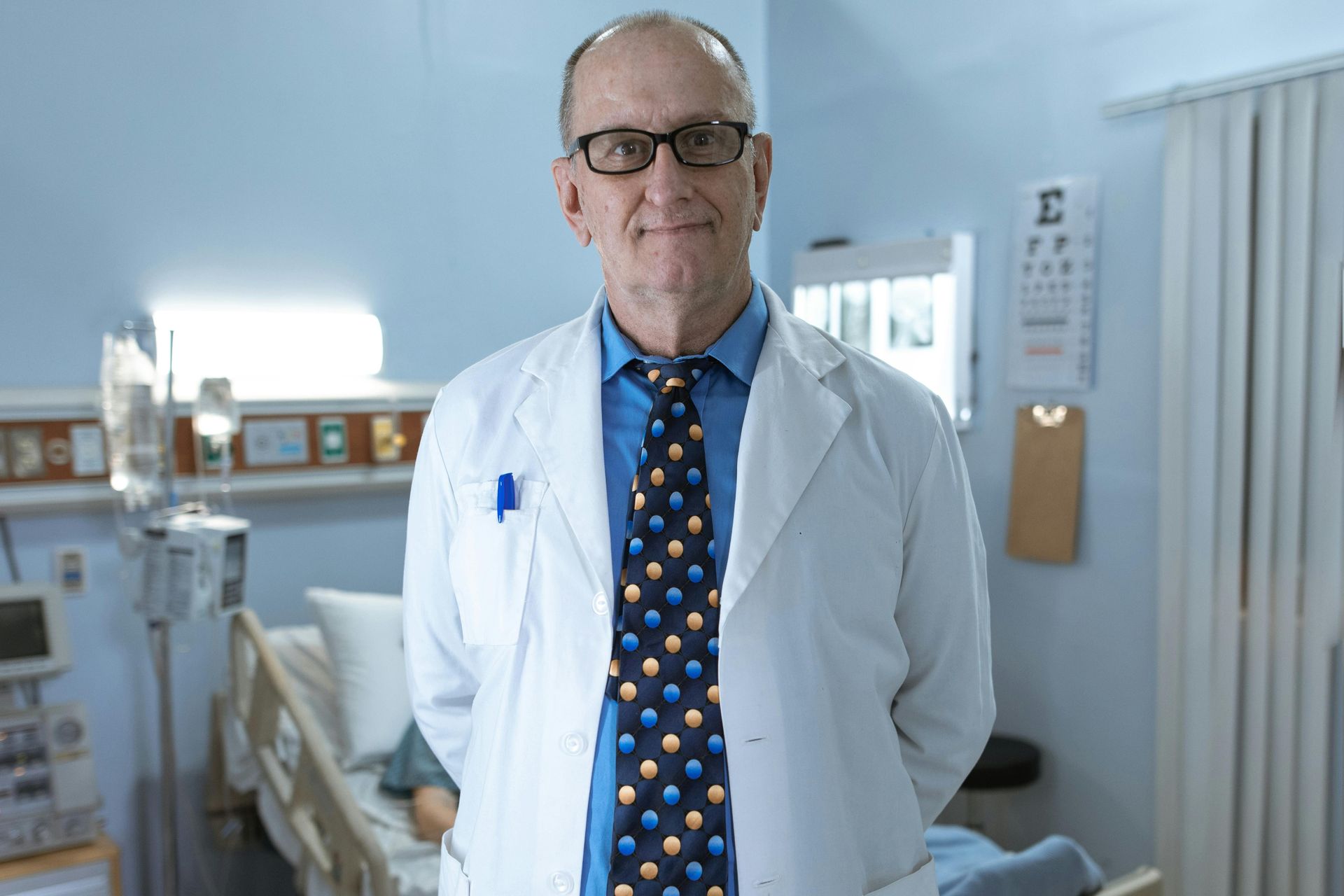 Doctor in a white coat and tie standing in a hospital room.