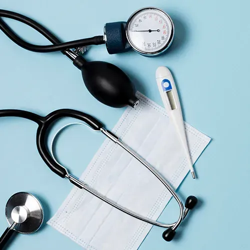 Blood pressure cuff, stethoscope, digital thermometer, and face mask on a light blue background