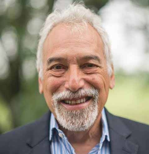 Smiling man with white hair and beard in a navy blazer outdoors
