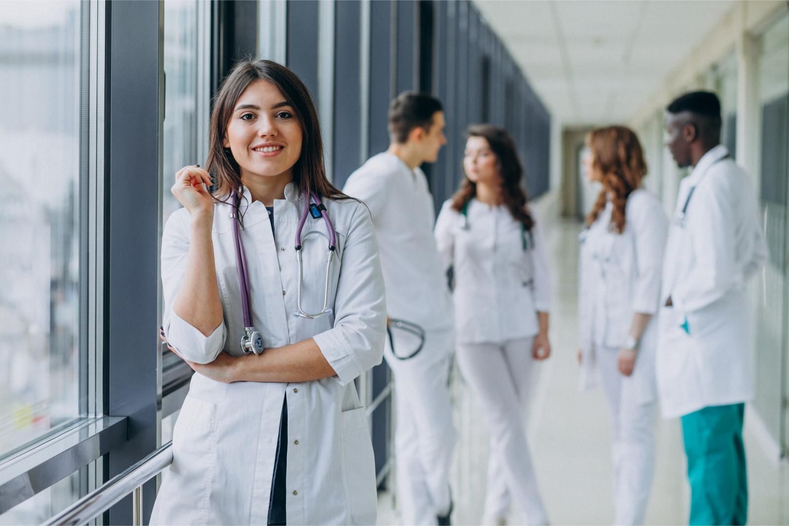 Doctors in white coats standing in a bright hospital corridor, with one smiling near a window