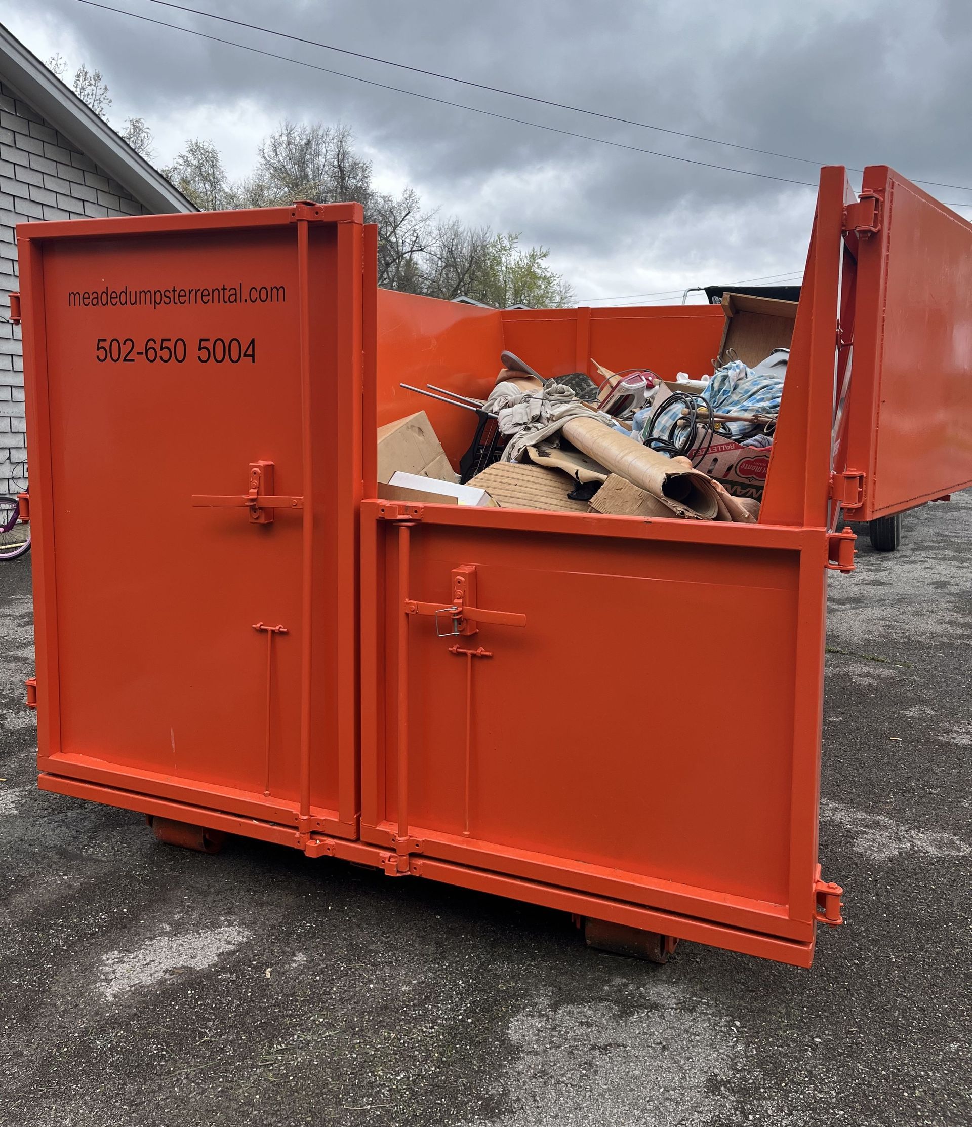 Orange metal dumpster filled with debris on a gravel lot under cloudy sky