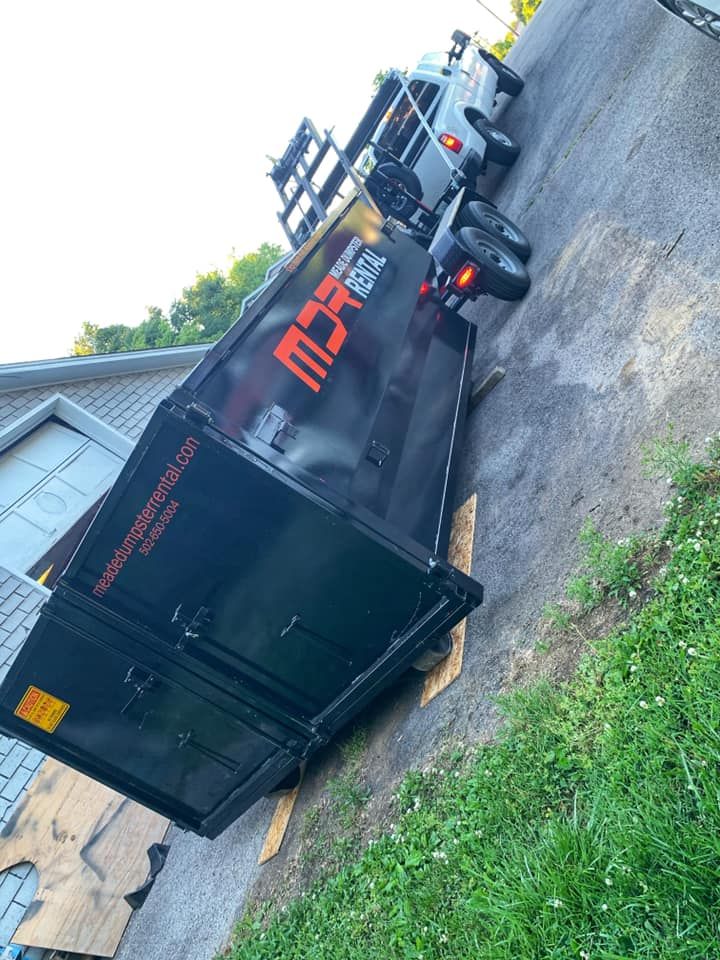 Black semi-trailer truck parked on a driveway beside a house, with an open lot in the background.