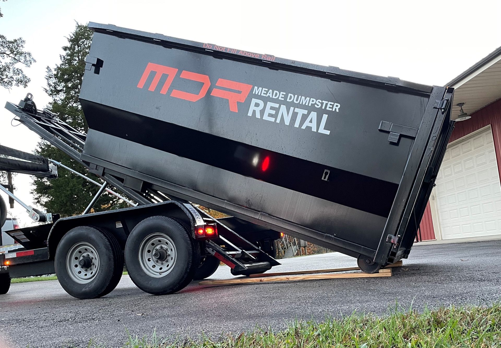 Large black dump trailer with red lettering, tilted on a paved driveway beside a building