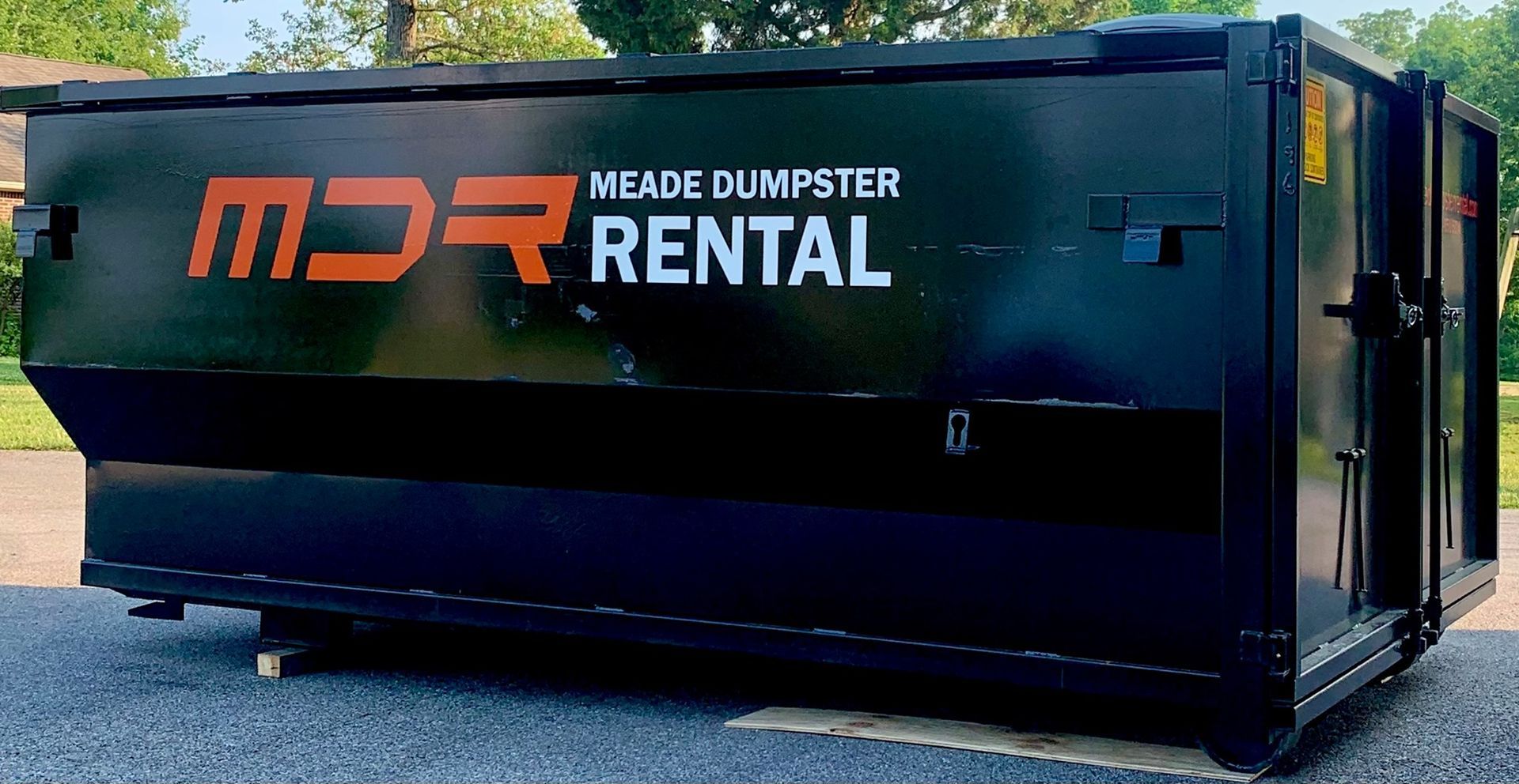 Black dumpster container with orange and white “MDR Equipment Rental” logo on gravel.