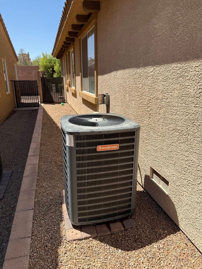 Air conditioning unit next to a stucco house, surrounded by gravel and a low brick border.