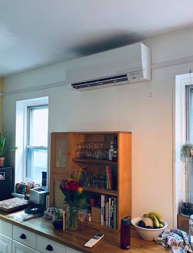 Air conditioner unit mounted above a wooden cabinet and countertop in a kitchen setting.
