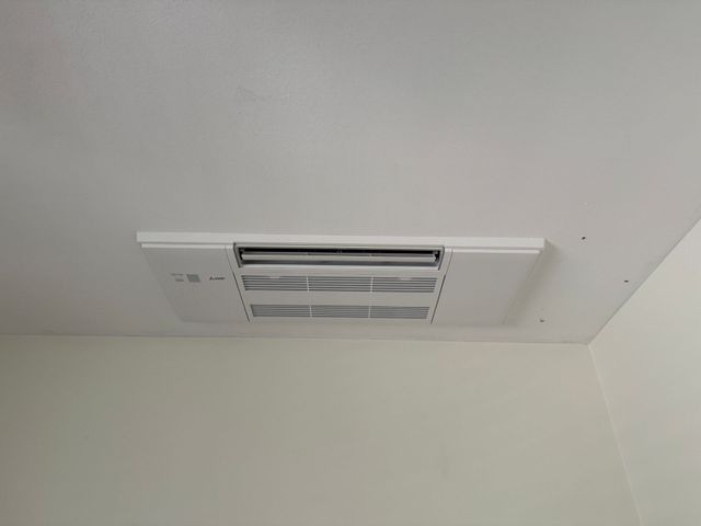 White ceiling-mounted air vent in a corner of a room with white walls.