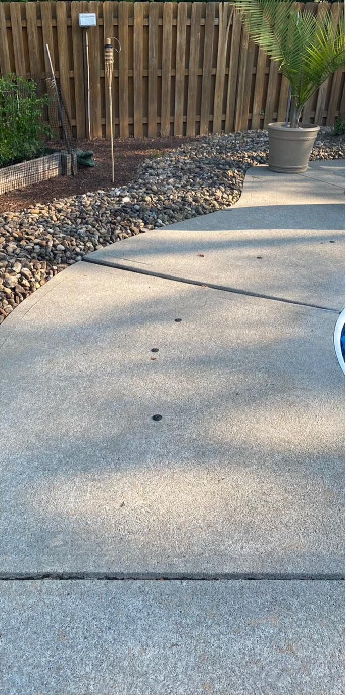 Concrete walkway next to a garden bed with rocks, fence, and a potted plant.
