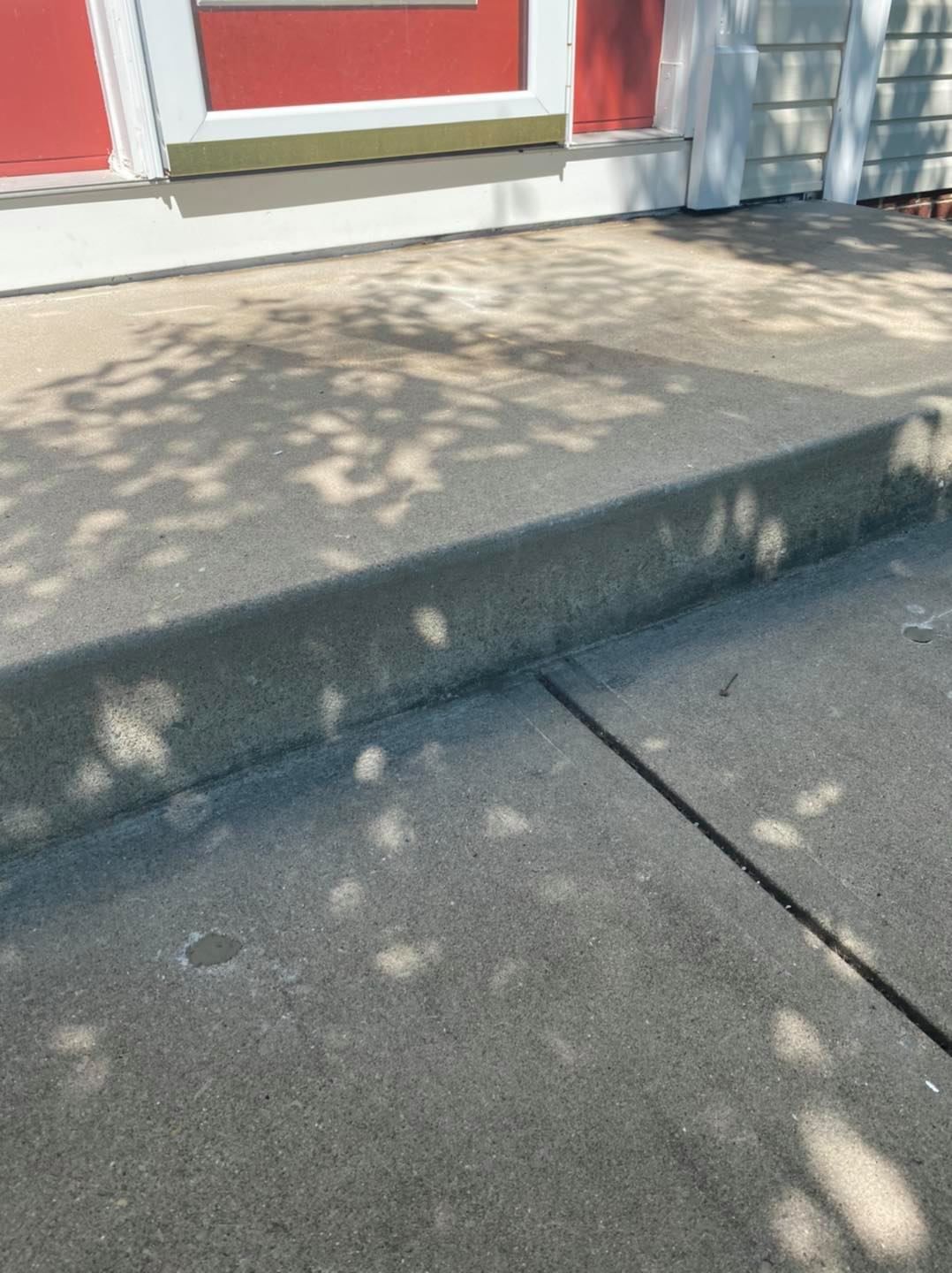 Concrete step leading up to a red door with tree shadows.
