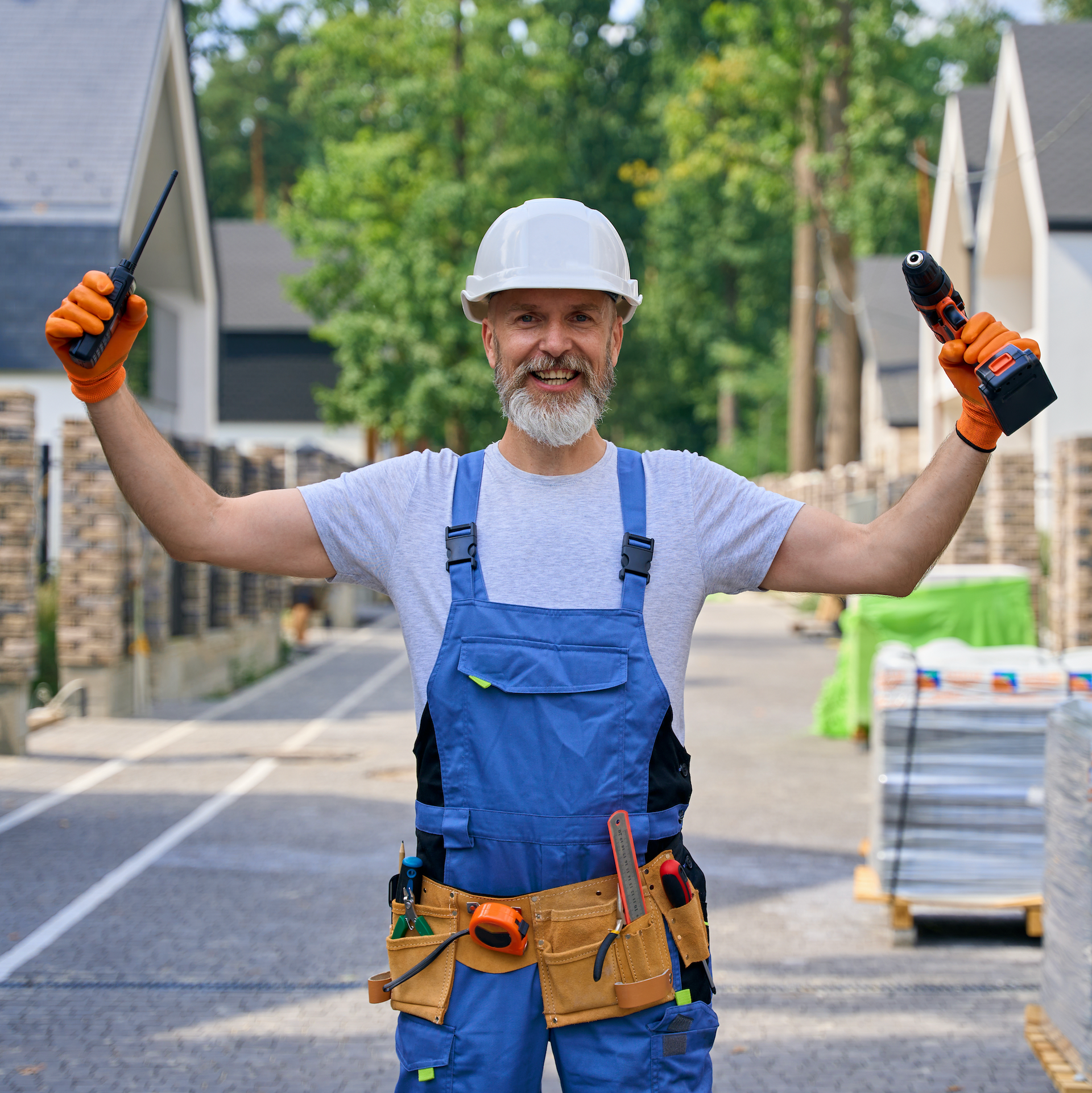 A trades man is holding up tools and smiling.