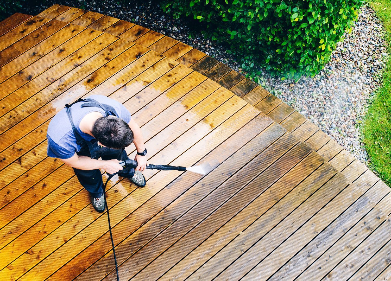 A man is cleaning a wooden deck with a high pressure washer.