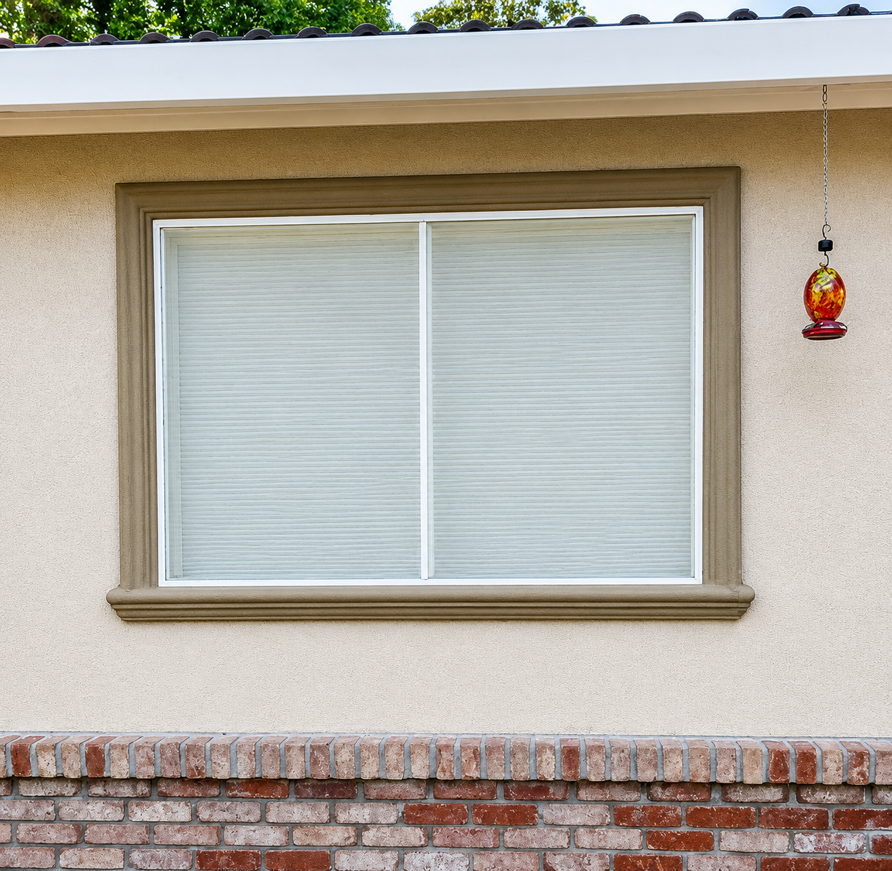 Exterior house wall with a large window and a small hanging lantern above a brick base