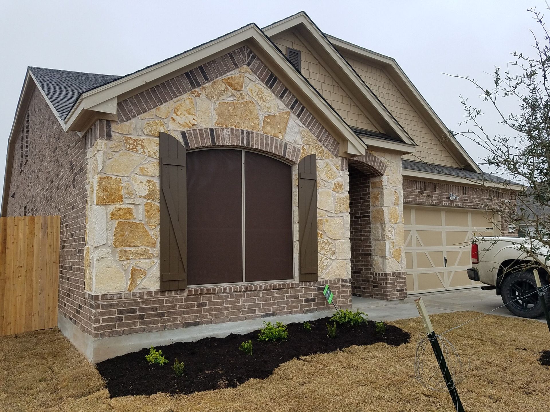 Suburban brick house with stone trim, covered windows, and a two-car garage under construction