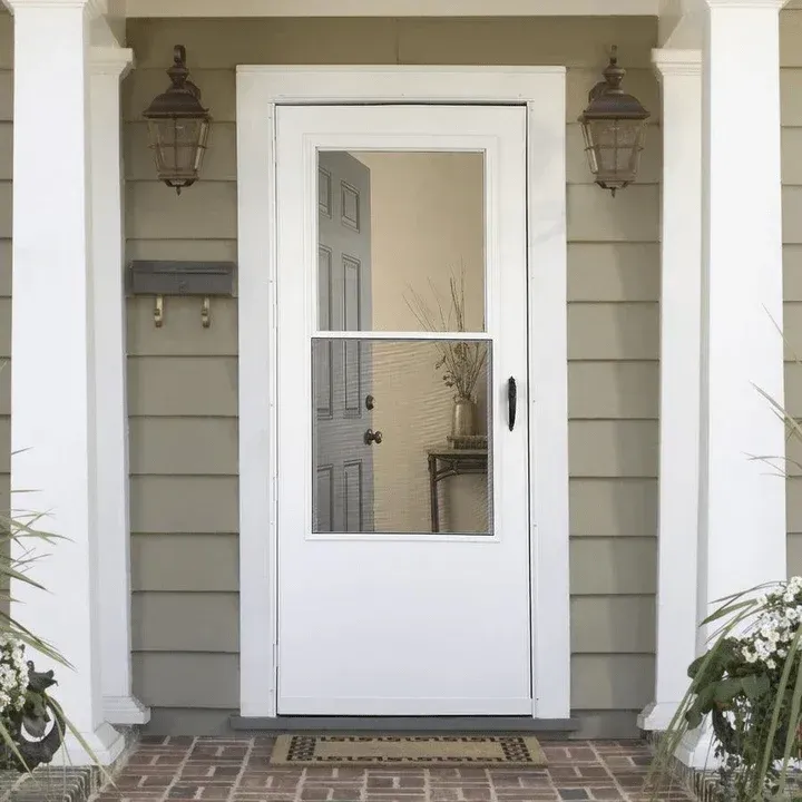 White front door with glass panel on a gray house porch, flanked by lanterns and columns