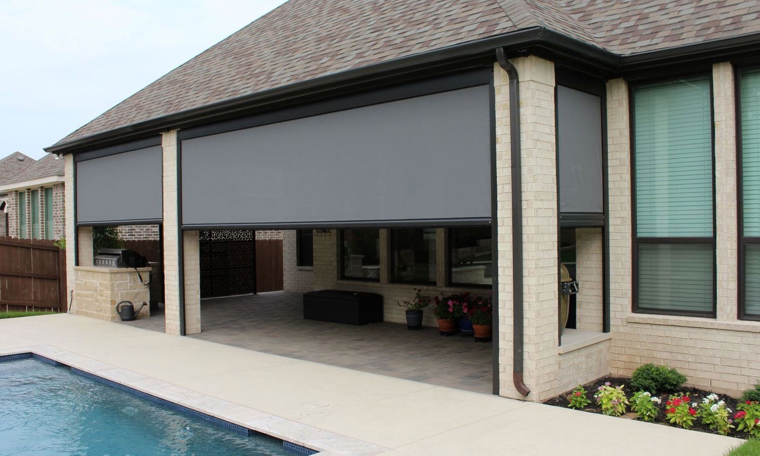 Backyard patio with a closed gray retractable screen in front of a poolside house
