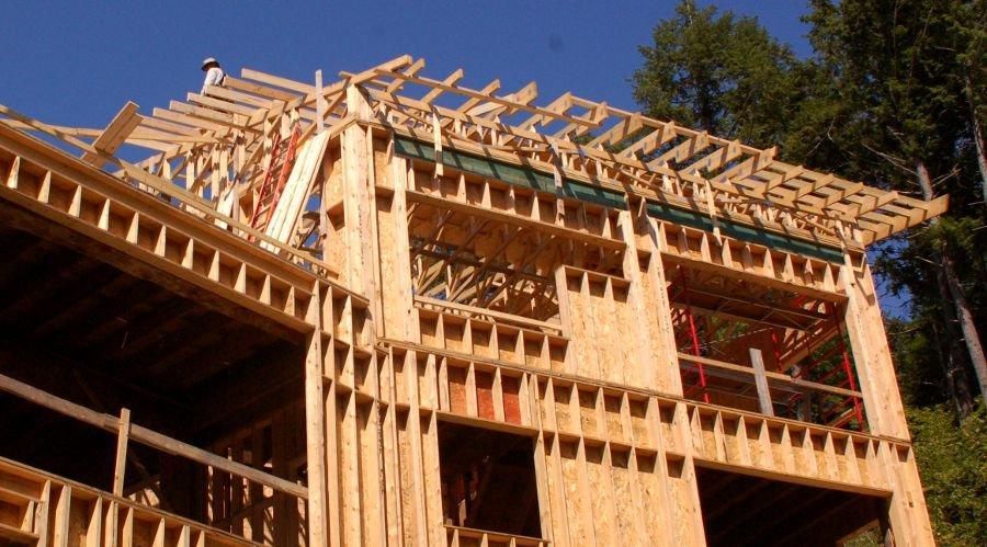 Wood-framed house under construction with exposed beams against a blue sky