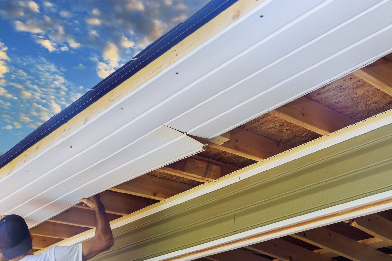 Close-up of house eaves with white soffit panels and exposed wooden rafters under a blue sky.