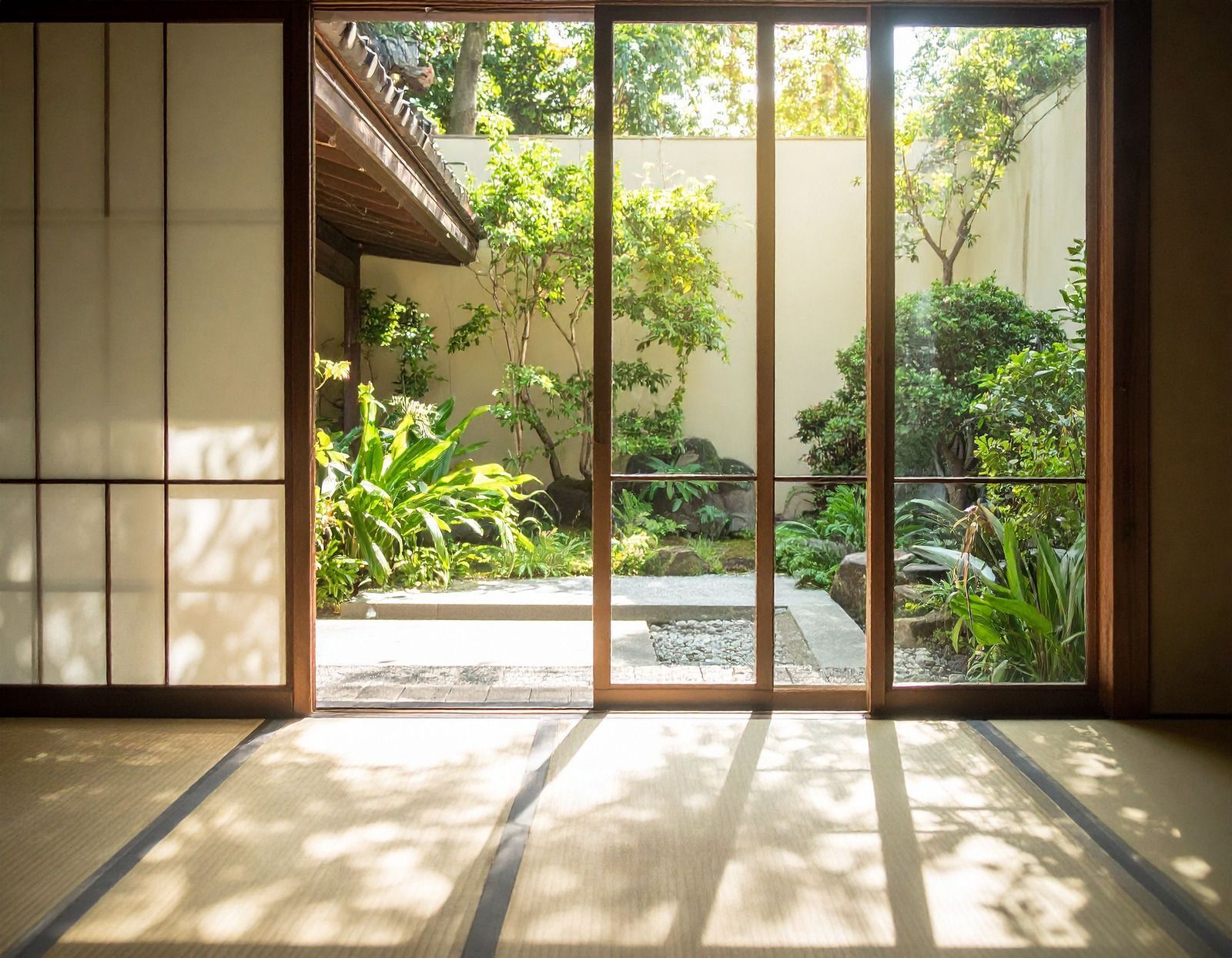 Sunlit Japanese-style room with sliding glass doors opening to a green courtyard