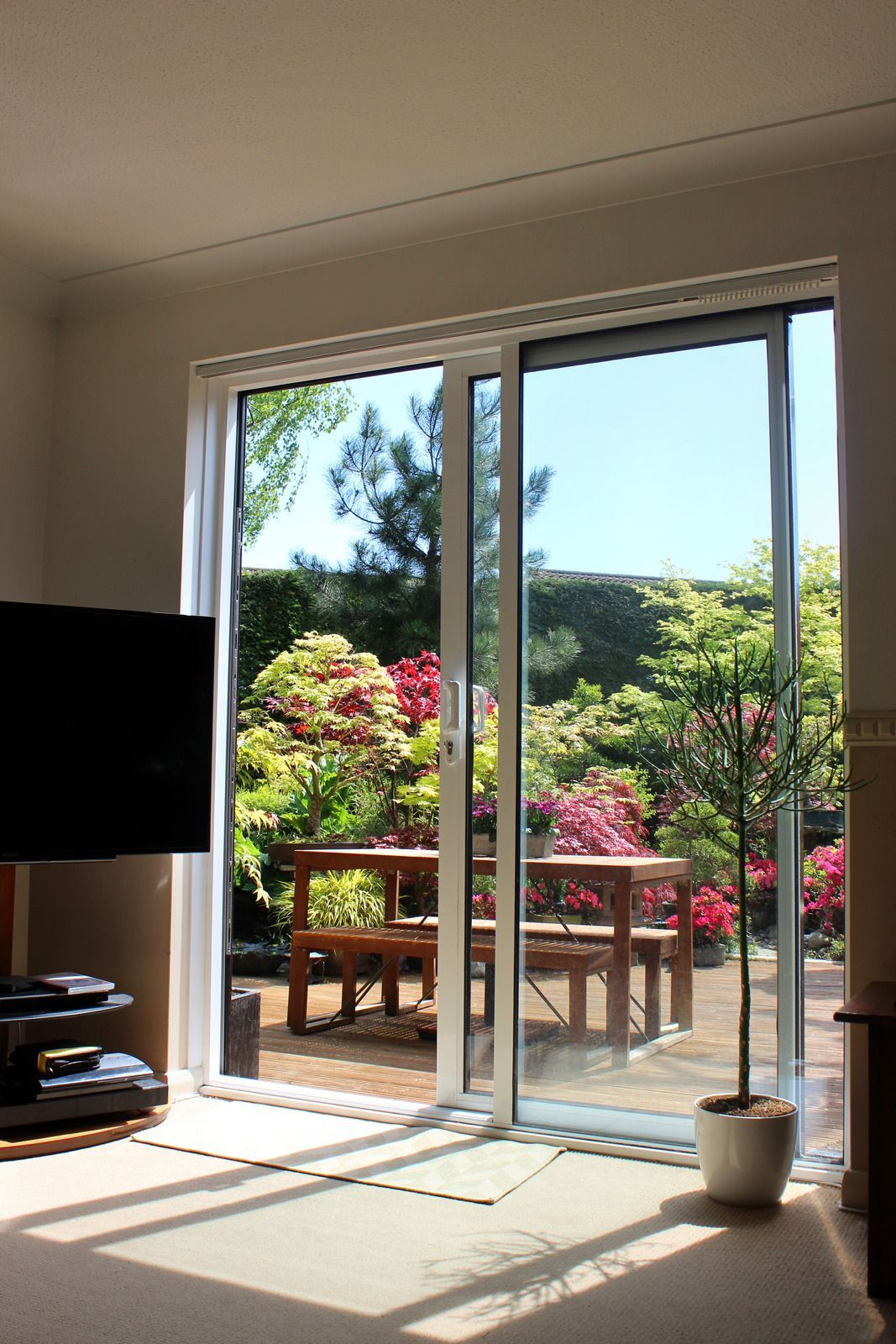 Sunlit living room with open sliding glass doors to a flower-filled patio and garden.