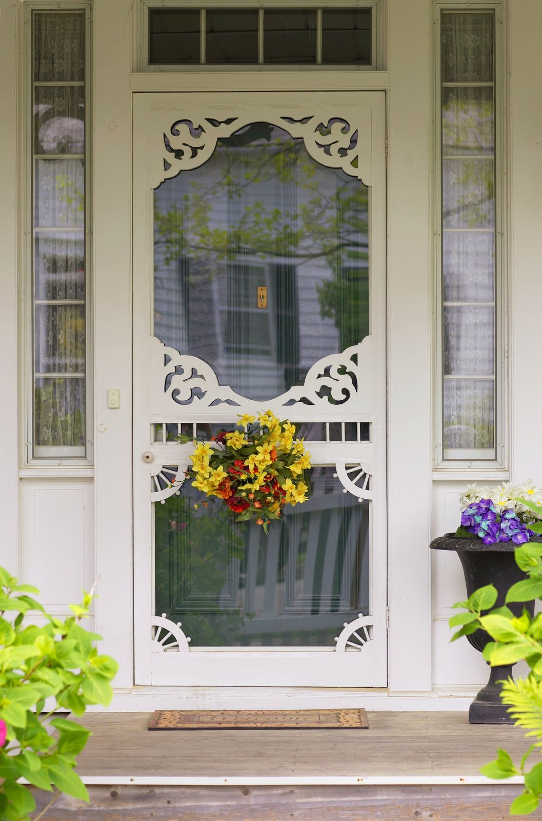 Decorative white front door with glass panel, wreath, and colorful flowers in pots on a porch