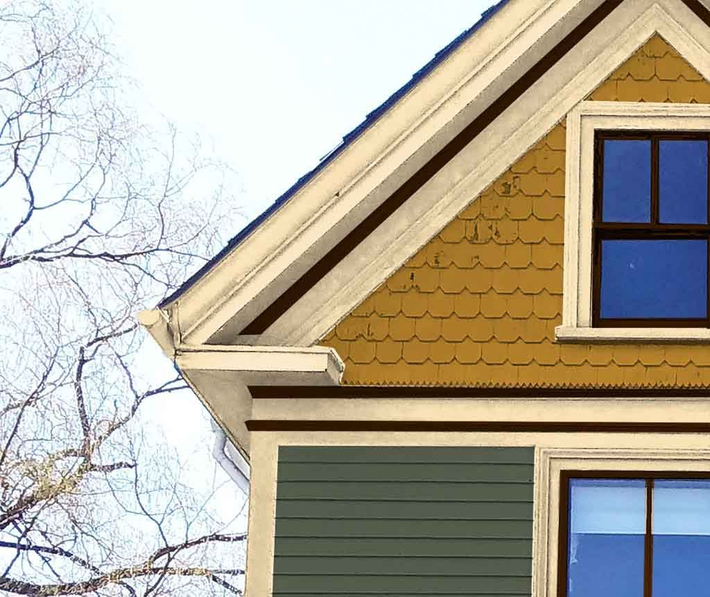 Corner of a tan house with green siding and blue windows under a sloped roof in winter