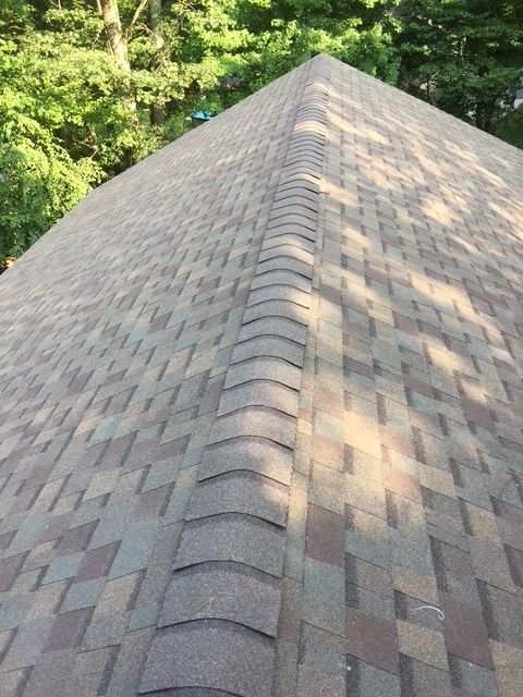 A close-up view of a brown and tan shingle roof with a central ridge.