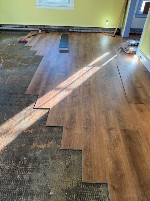 Installing laminate flooring in a room with yellow walls. Partially installed, revealing the old floor.