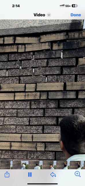 Person looking up at a weathered brick wall, overcast day.