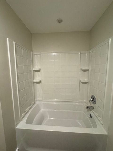 White, tiled shower enclosure with built-in tub and shelves, chrome faucet, beige walls.