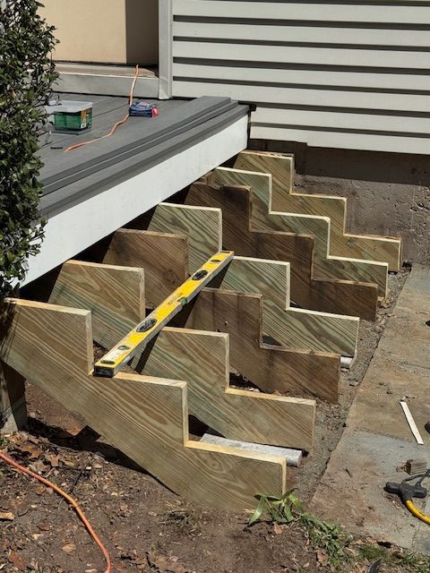 Wooden steps under construction, a level is placed across the steps. Outdoors, near a house.