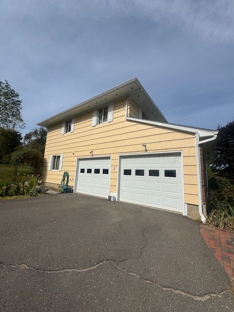 Yellow two-story house with two white garage doors, a driveway, and a cloudy sky.