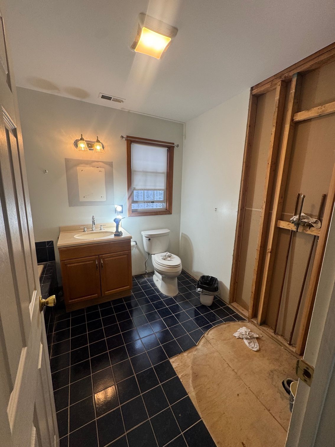 Bathroom under renovation, with exposed framing, vanity, toilet, and black tile flooring.