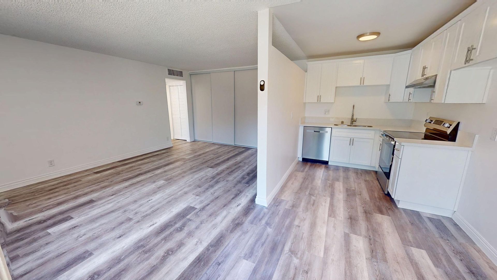 Interior view of a kitchen and living area with white cabinets, gray wood floors, and neutral walls.