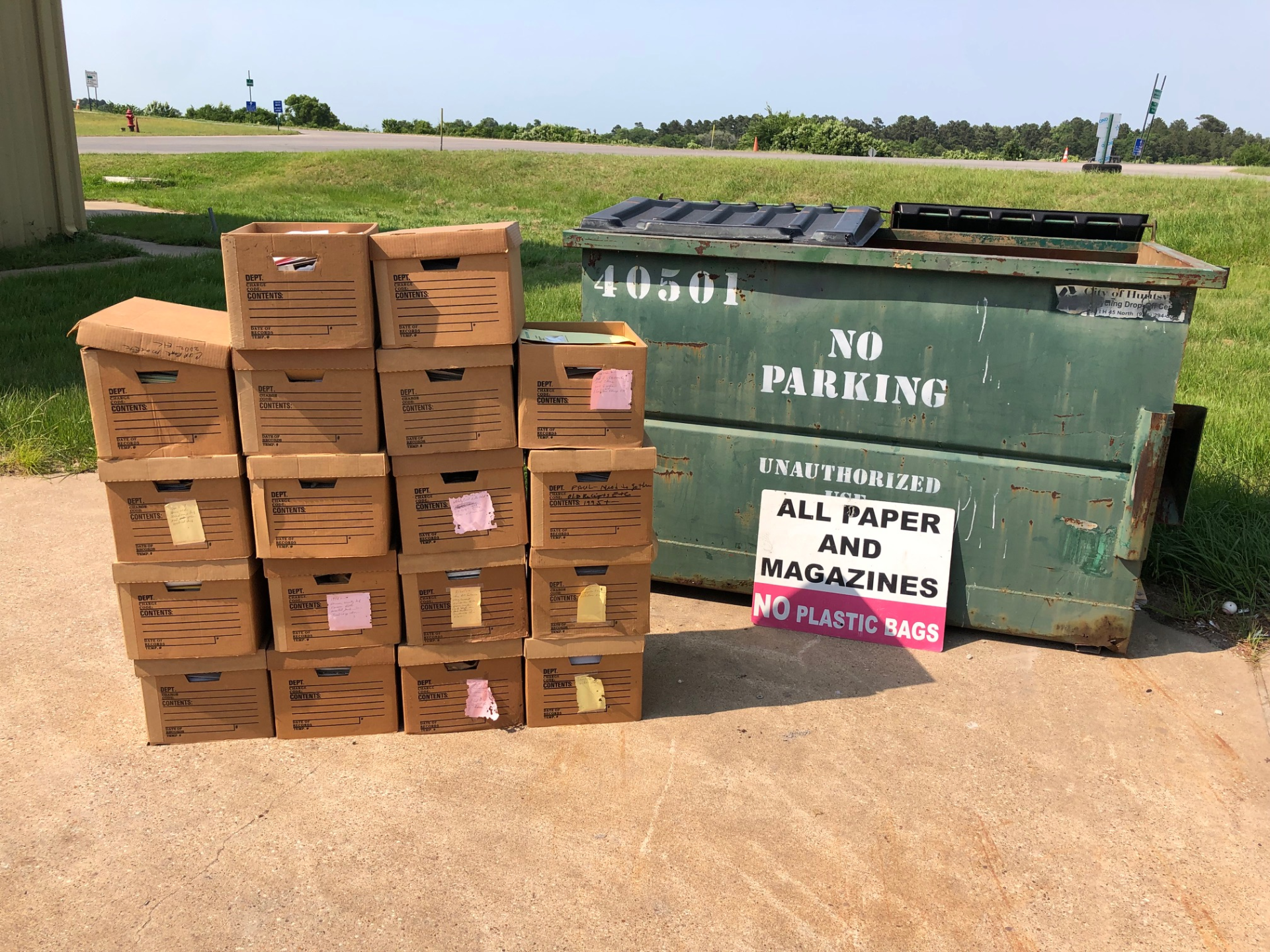 pile of boxes with papers and magazines beside a dumpster