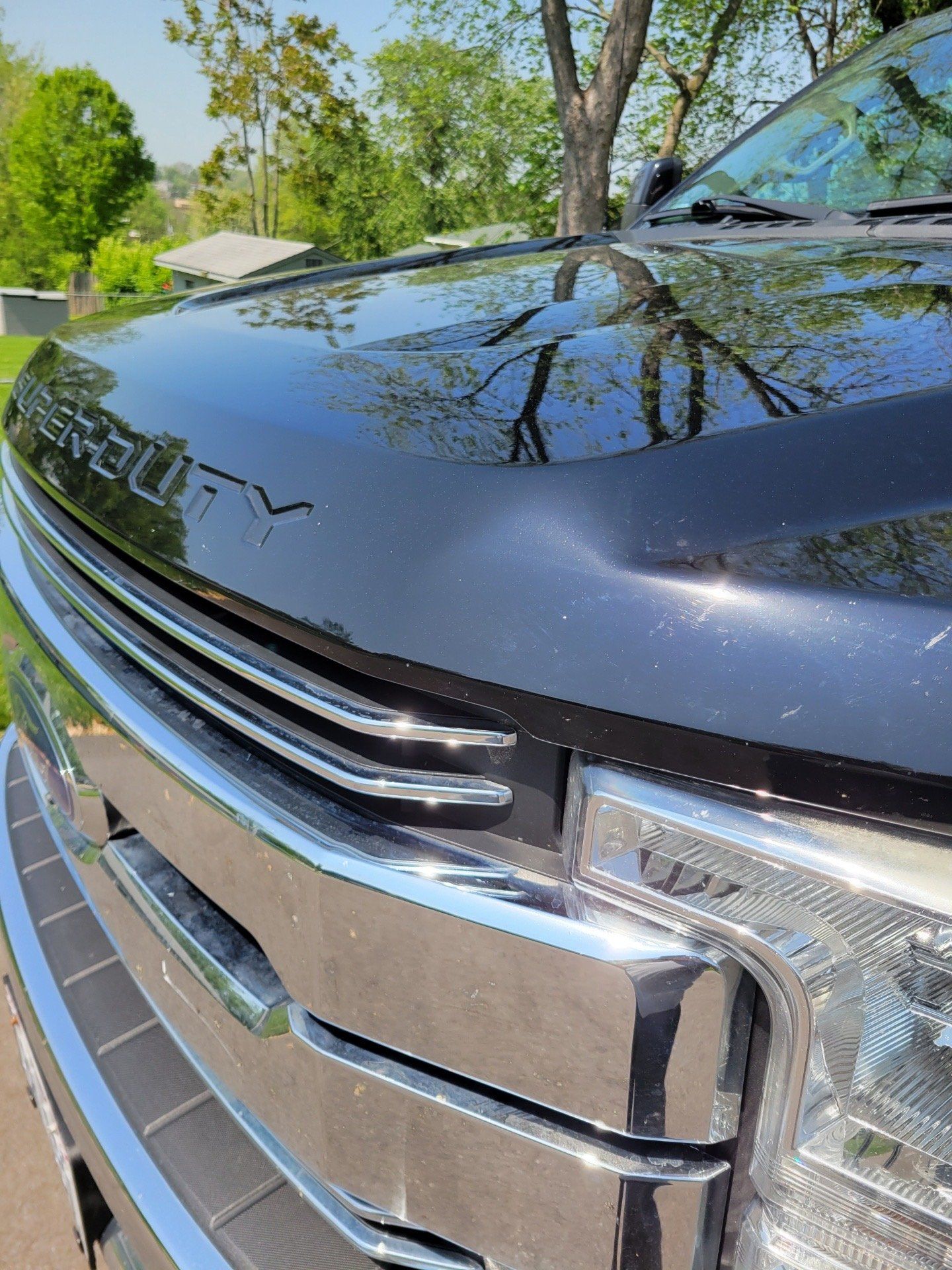 Close-up of a black truck grille and headlight reflecting trees and sky outdoors
