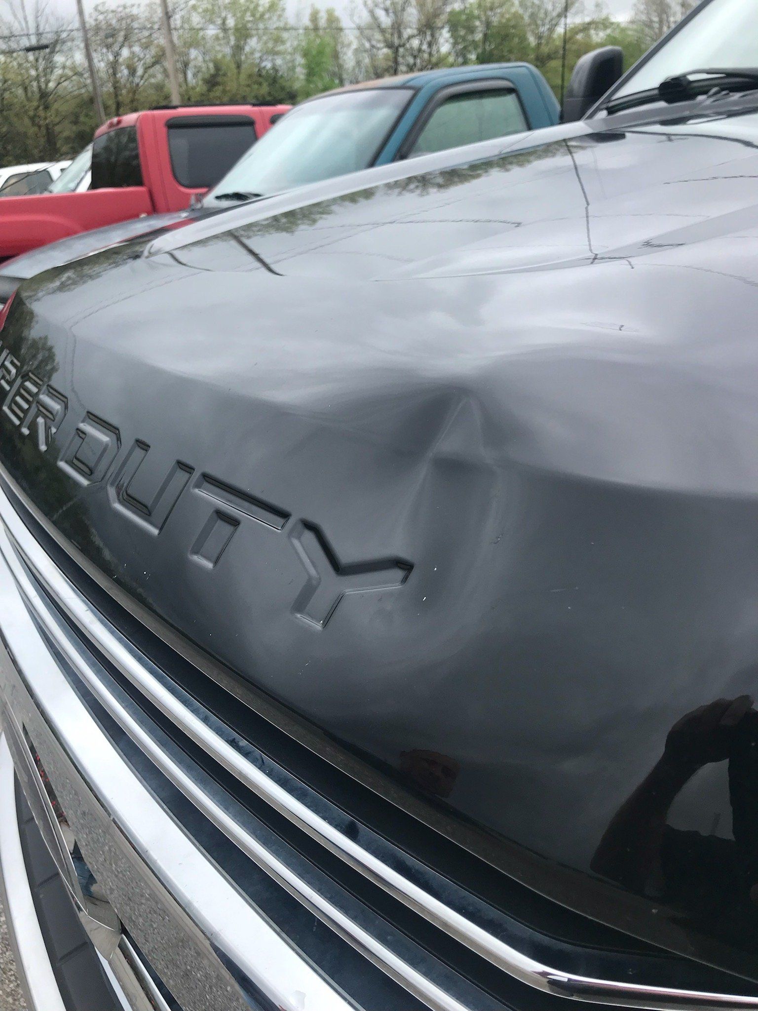 Close-up of a black Chevrolet truck hood and grille, with a red pickup parked behind it.