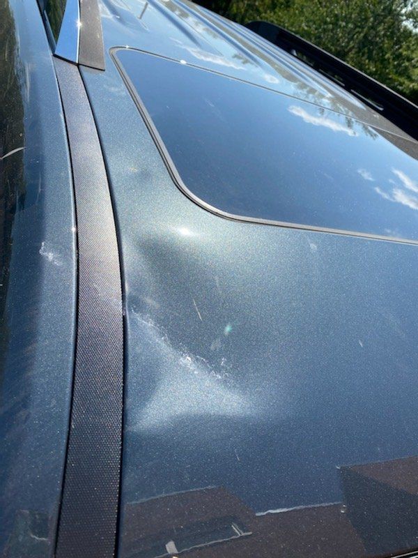 Close-up of a dark car roof with a sunroof and visible dust specks.