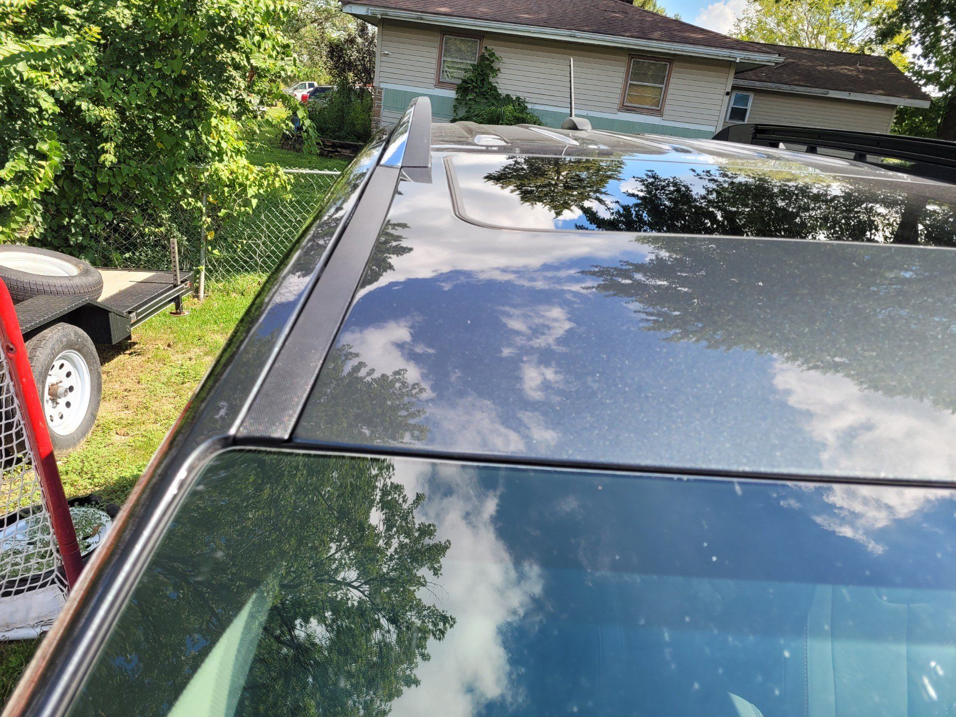 Car roof with a long black roof rack beside a driveway and house