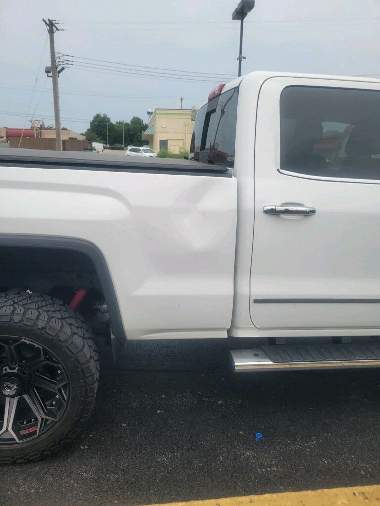 White pickup truck parked on wet pavement, side view with black off-road tires.
