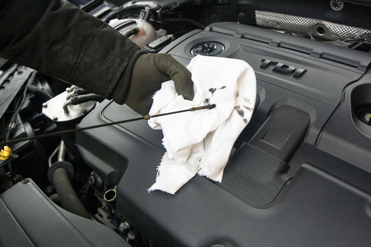 Mechanic wiping an engine dipstick with a white cloth inside a car hood
