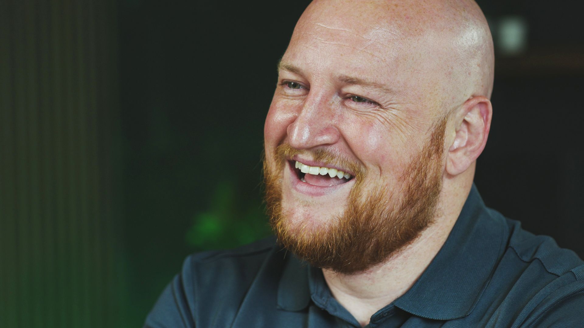 A bald man with a red beard is smiling.