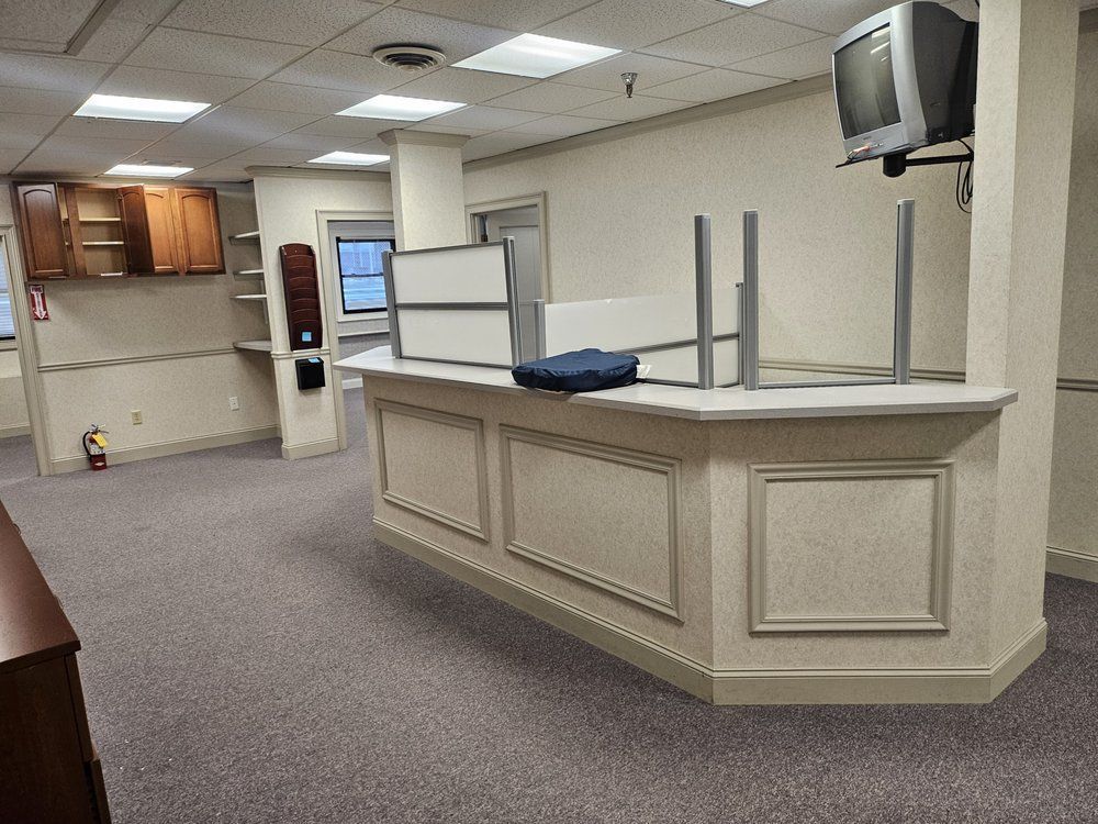 Empty reception desk in a carpeted office lobby with beige walls and a wall-mounted TV.