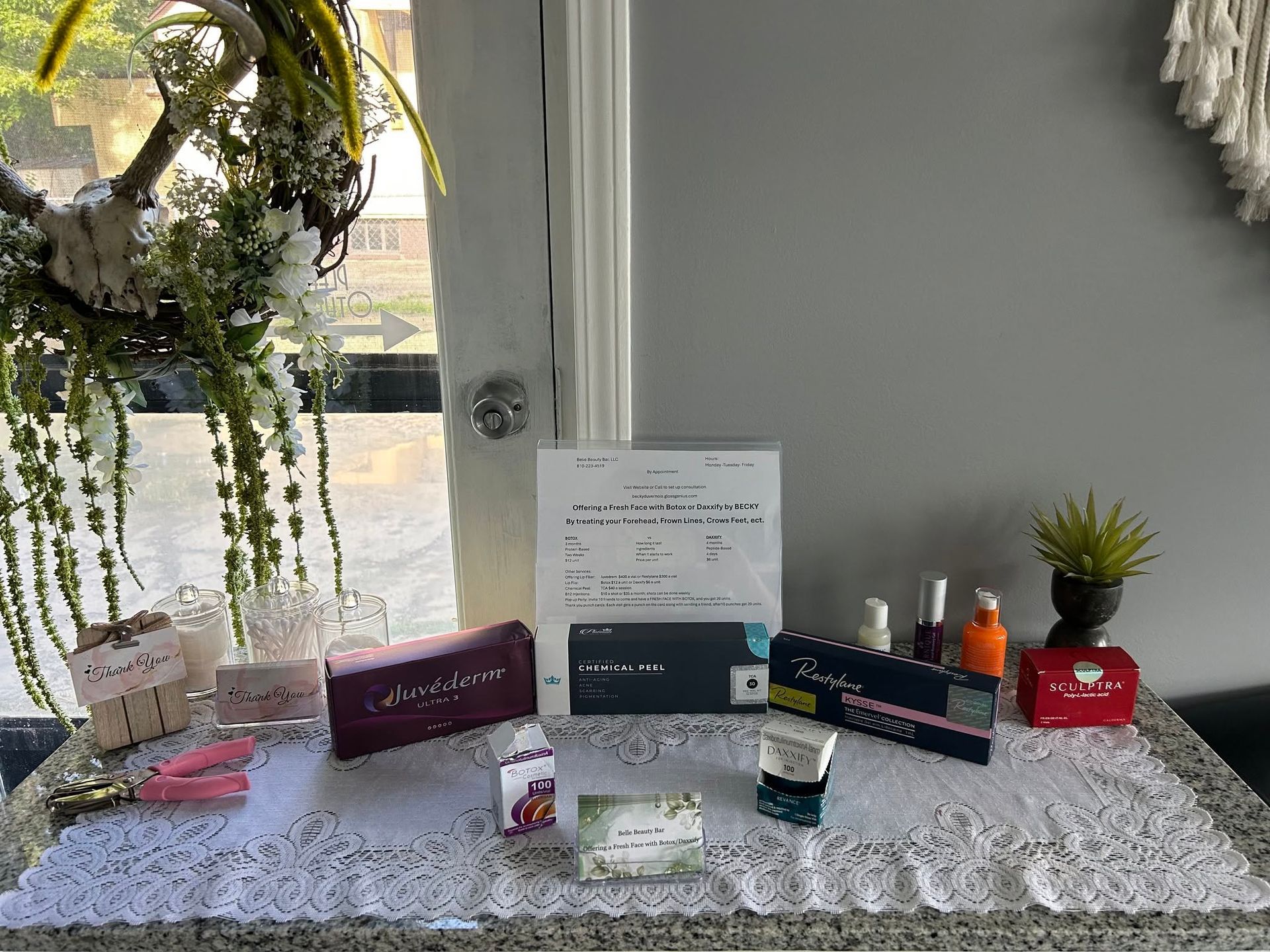 Award display on a white table with certificates, plaques, small plants, and decorative items by a window.