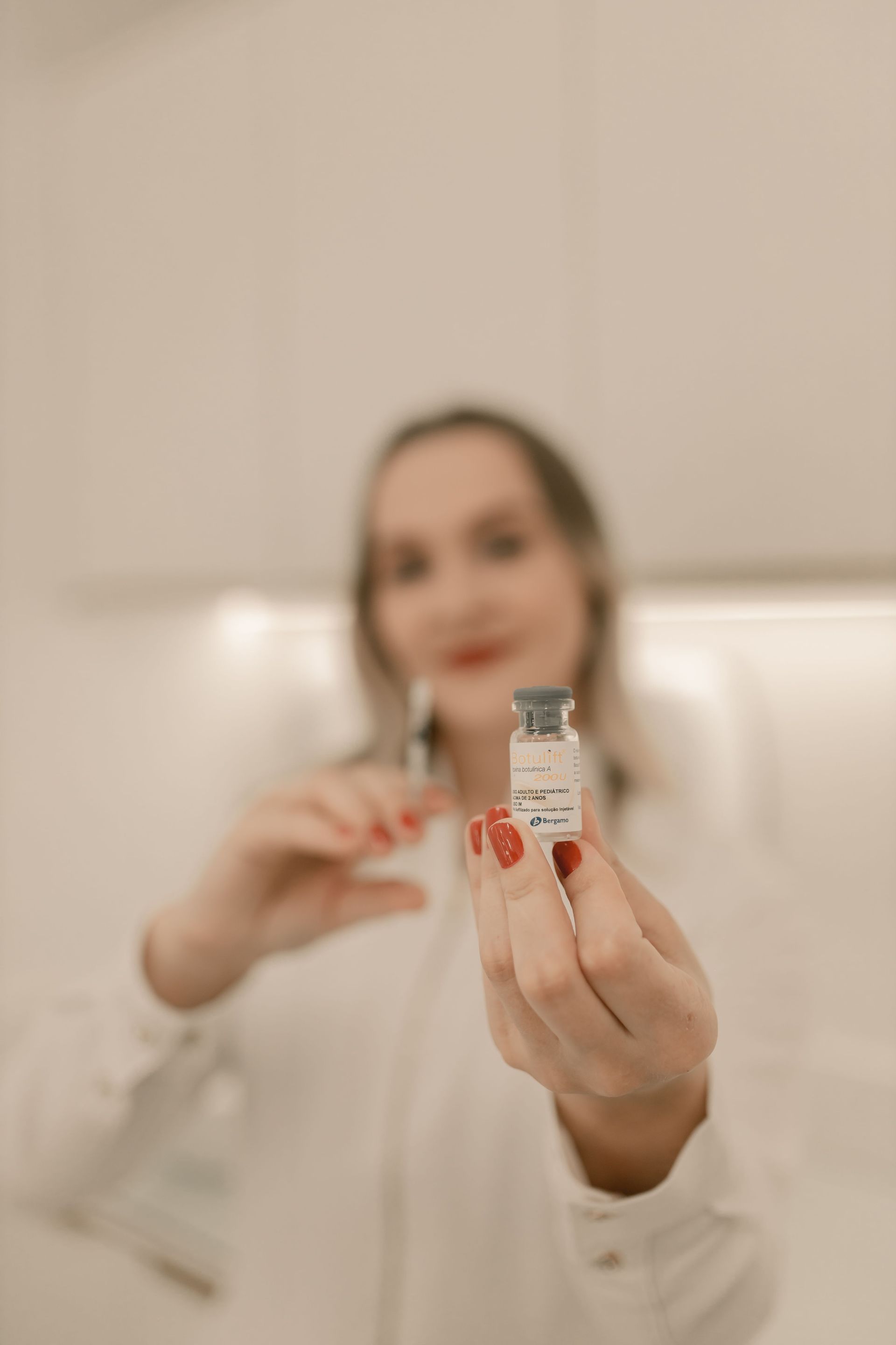 Hand holding a small vial with a blurred woman in the background