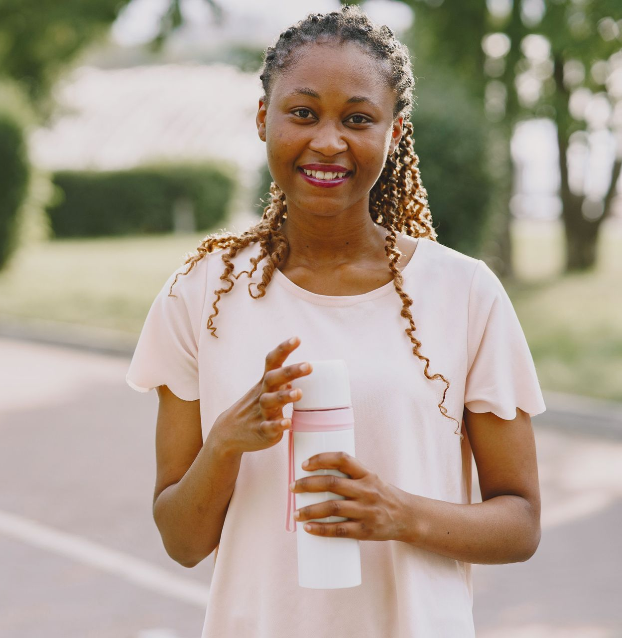 Smiling person holding a white water bottle outdoors on a tree-lined path