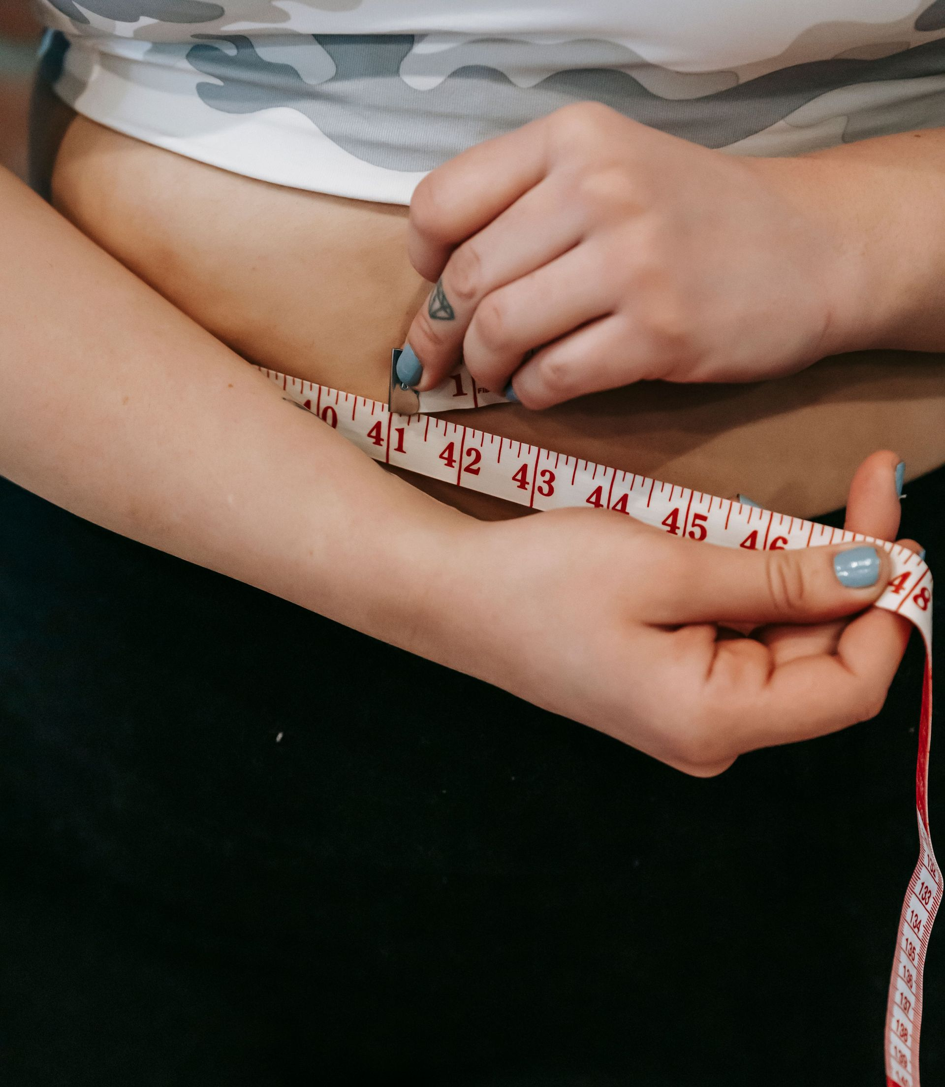 Hands measuring a waist with a white measuring tape against a light shirt and dark background